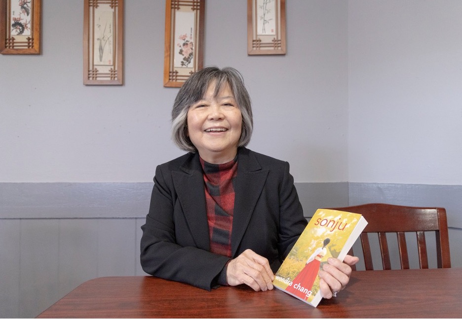 Wondra Chang smiling and holding a copy of her novel Sonju
